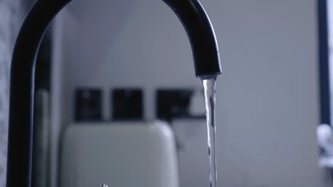camera approaches water tap on slider until water stream is in focus as water gushes out. clean, modern, grey kitchen.