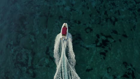 cámara lenta, disparo aéreo sobre un bote de velocidad con un techo rojo que pasa a través de un mar mágico de color turquesa claro.