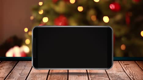 Animation-of-blank-smartphone-screen-with-out-of-focus-christmas-tree-on-wooden-surface