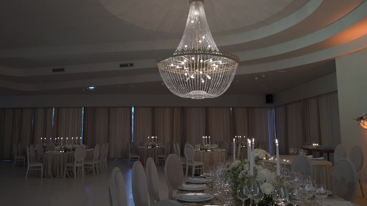 Spacious wedding hall with a grand chandelier, round tables, and candlelit decor