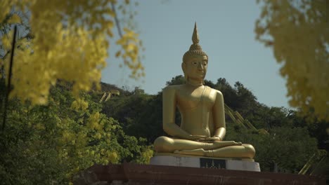 a golden seated buddha image surrounded by yellow flowers