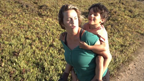 happy mom piggybacking kid, walking on mountain path