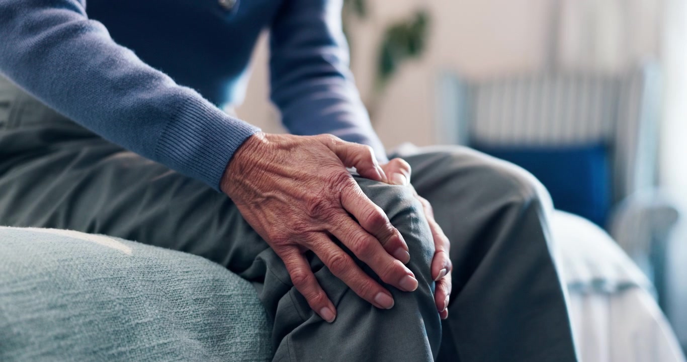 Persona anziana seduta con la mano sul ginocchio dolorante