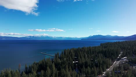 Drone-flyover-down-the-coastline-of-Lake-Tahoe-with-blue-sky-and-sun