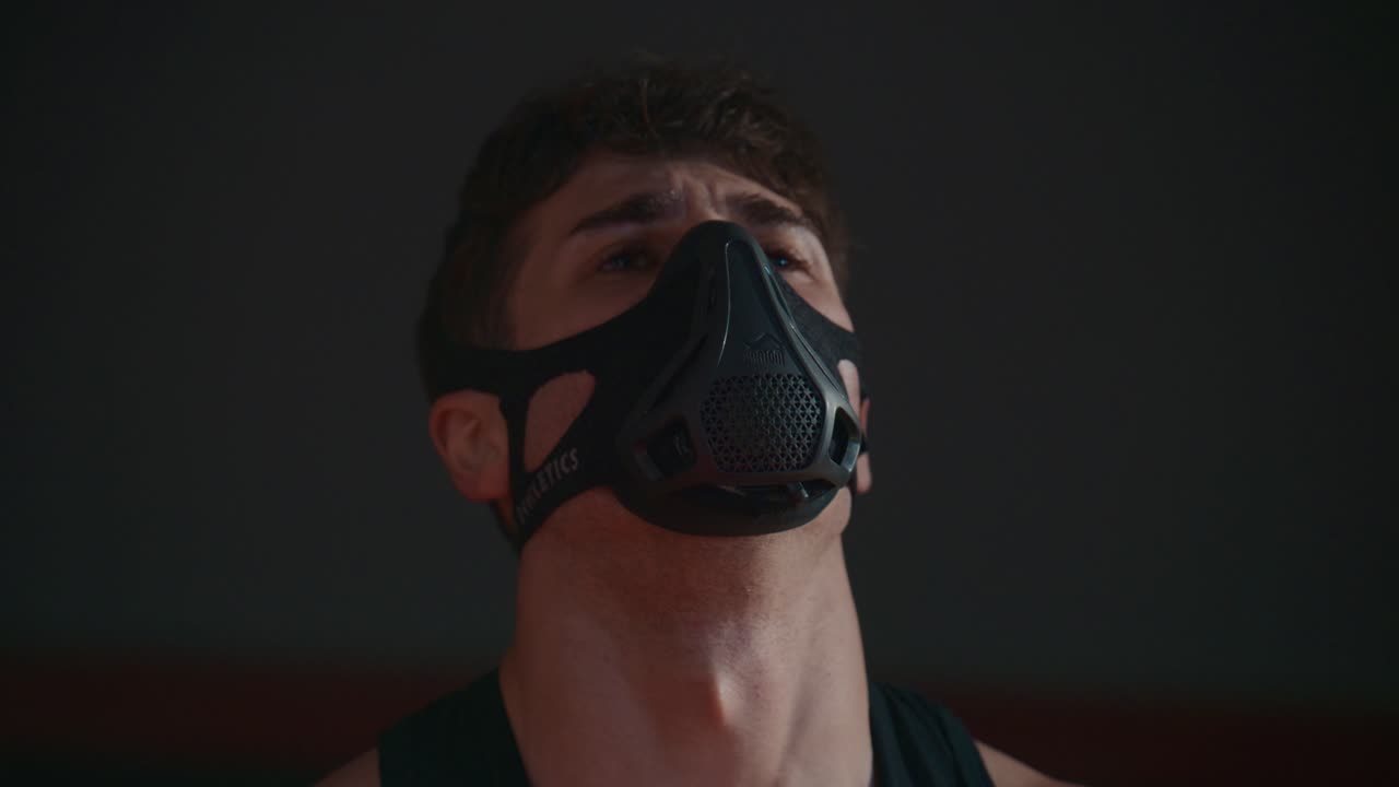 Joven con máscara de entrenamiento respirando con dificultad en el gimnasio.