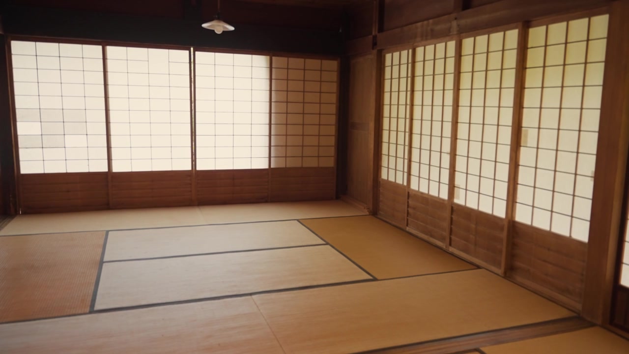 Raggi di sole che filtrano attraverso schermi shoji in carta washi in una tradizionale stanza giapponese, mettendo in risalto gli intricati dettagli in legno e il pavimento in tatami di uno spazio abitativo tranquillo e vuoto