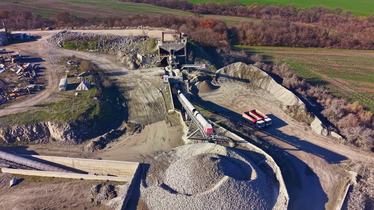 Industrial site bustling with activity as machinery processes gravel and stone against a backdrop of rolling fields