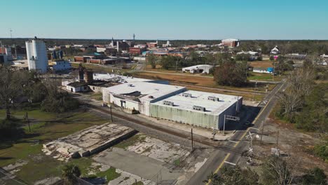 A Large Industrial Facility With Towering Storage Silos Stands Beside Railroad Tracks in a Small City - Aerial Drone Shot