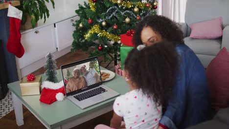 Happy-african-american-mother-and-daughter-on-video-call-on-laptop-with-grandparents-at-christmas