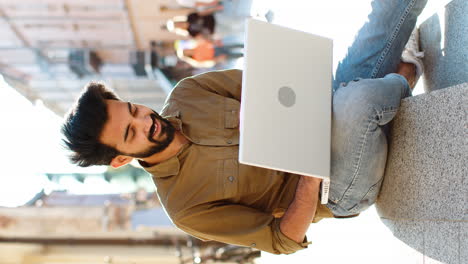 indian man freelancer working online distant job with laptop sitting in city street browsing website