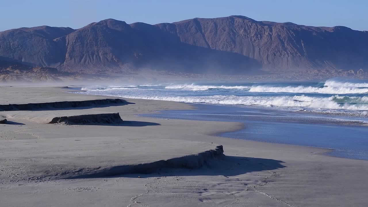 la arena sopla de las montañas del desierto de atacama sobre las olas de la playa del océano, chile