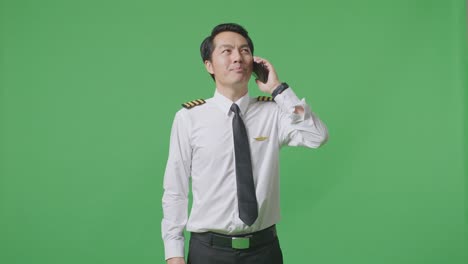 asian man pilot talking on smartphone and looking around while standing in the green screen background studio