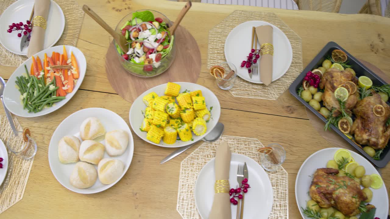 Camera is panning right across set wooden table revealing roast chickens, salad, sliced baguette