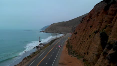 establishing drone shot as car pulls out onto pacific highway one, near malibu on a grey and foggy morning