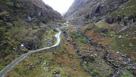 Toma-Cinematográfica-De-Un-Dron-Moviéndose-A-Través-De-La-Brecha-De-Dunloe,-Irlanda,-A-Través-De-Las-Paredes-Rocosas-Del-Acantilado-Con-Una-Carretera-En-El-Valle.