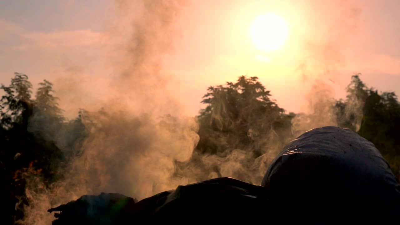 서서히 움직이는 불은 해가 뜨면 어두운 배경에서 쓰레기 봉투를 태우고 공기 오염과 위험한 환경으로 떠다니는  연기가 쓰레기입니다. 쓰레기는 공동체의 폐기물입니다. 그것은 지구의 온실 효과를 만니다.