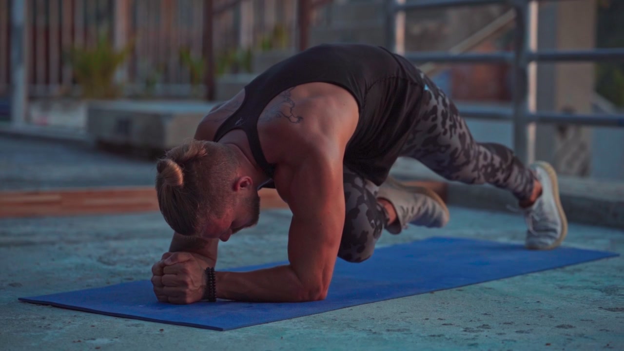 Uomo atletico che esegue plank con ginocchia al petto su un tappetino da yoga