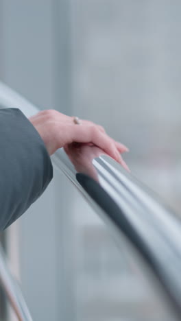 primer plano de la mano de la dama adornada con un anillo colocado en el riel de la escalera mecánica descendente con vidrio en el fondo que muestra el paisaje al aire libre a través del vidrio en un entorno urbano brillante