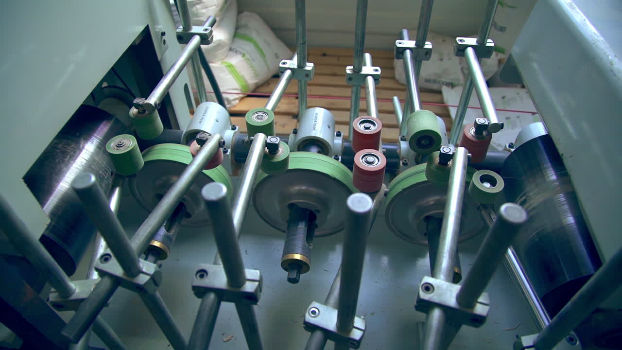 Metal rollers spin and move the timber bar along the conveyor. Door manufacturing equipment at modern plant.