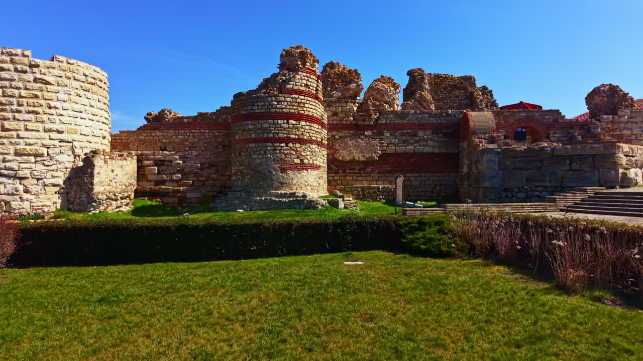Rovine di un'antica struttura in uno spazio esterno soleggiato che mostra muri in pietra e terreno erboso