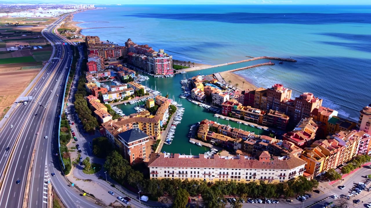 Città turistica costiera e mare, Castellón, Spagna. Angolazione aerea elevata di un canale d'acqua turchese, autostrada, spiaggia sabbiosa, hotel colorato e oceano blu profondo.