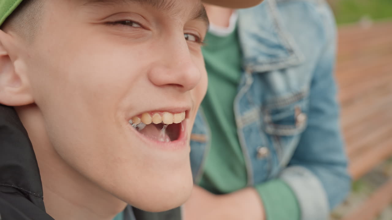 White Teenage Boy Sits On Bench With DenimJacket Friend, CloseUp Portraits Showing Cap, Pensive Expression And Supportive Arm, Candid Outdoor Park Scene Conveying Vulnerability, Listening