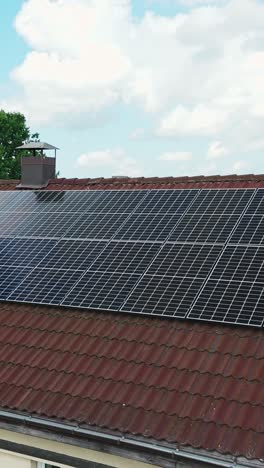 Vertical drone pull-out reveals a photovoltaic array spanning a terracotta tile roof, highlighting clean renewable energy under a blue sky