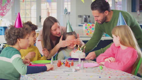 girl blowing out candles on birthday cake at party with parents and friends at home