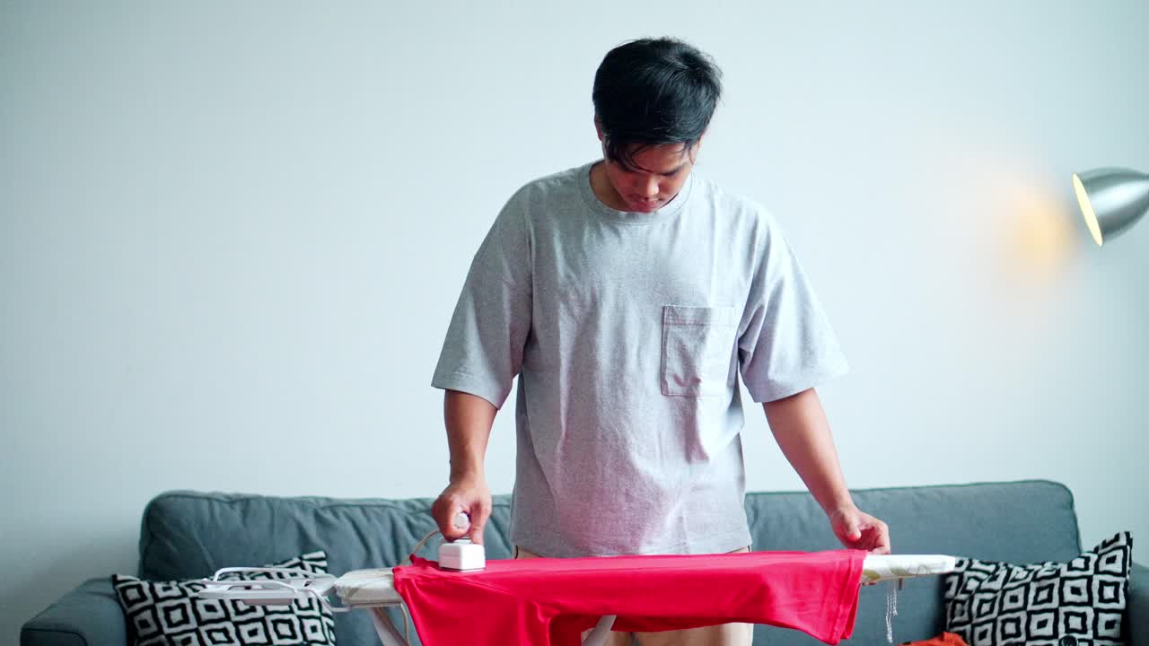 Responsible man doing his domestic duties pressing clothes on ironing board at home. Modern independent lifestyle
