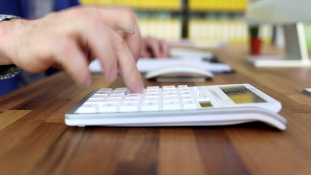 Mano di contabile che scrive dati su carta e calcola con la calcolatrice in ufficio, primo piano, video 4k