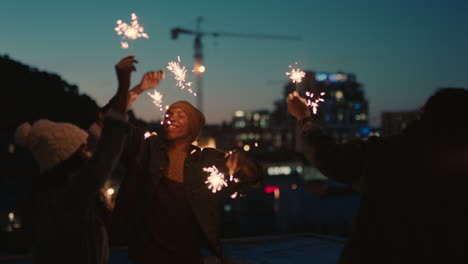 happy friends holding sparklers celebrating new years eve on rooftop at sunset having fun enjoying holiday party celebration