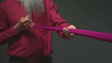 Close-Up-Low-Key-Studio-Lighting-Shot-Of-Senior-Sikh-Man-Folding-Fabric-For-Turban-Against-Plain-Dark-Background-Shot-In-Real-Time