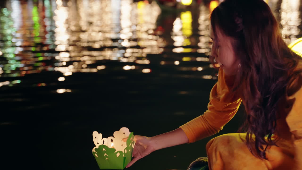 Em câmera lenta, uma mulher vietnamita em traje tradicional colocando um barco de papel com vela no rio à noite em Hoi An, Vietnã.