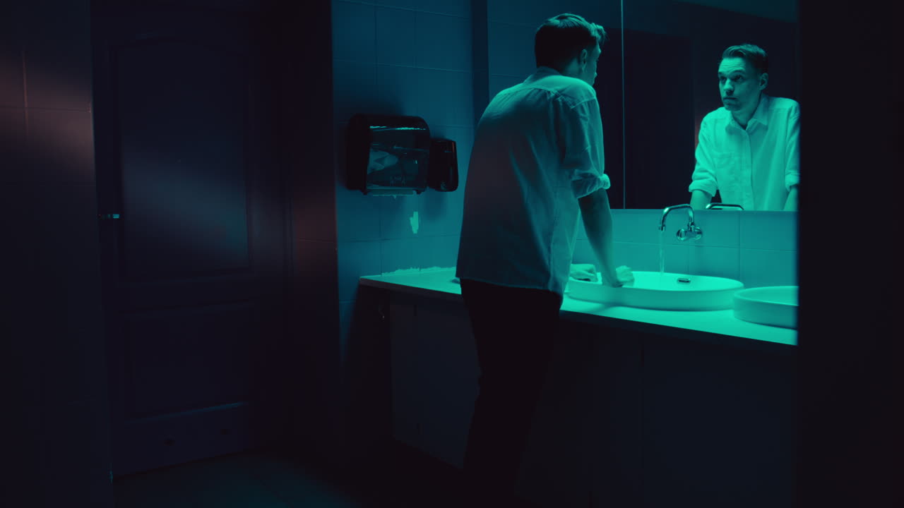 Man Washing Hands in a Dark Bathroom