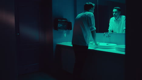 man washing hands in a dark bathroom