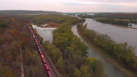 Vista-Aérea-Del-Tren-De-Carga-Con-Cientos-De-Transportes-De-Automóviles-A-Través-De-Los-Bosques-Otoñales-De-Illinois