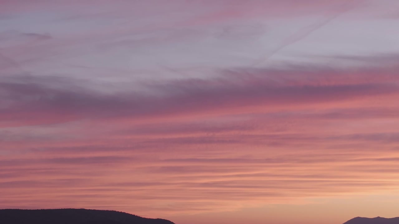 Ascesa di drone con teleobiettivo a 167 mm che rivela uno spettacolare tramonto sopra la Catena Montuosa Centrale, dove tonalità calde di giallo, arancione e rosso sfumano gradualmente in cieli viola e blu intenso