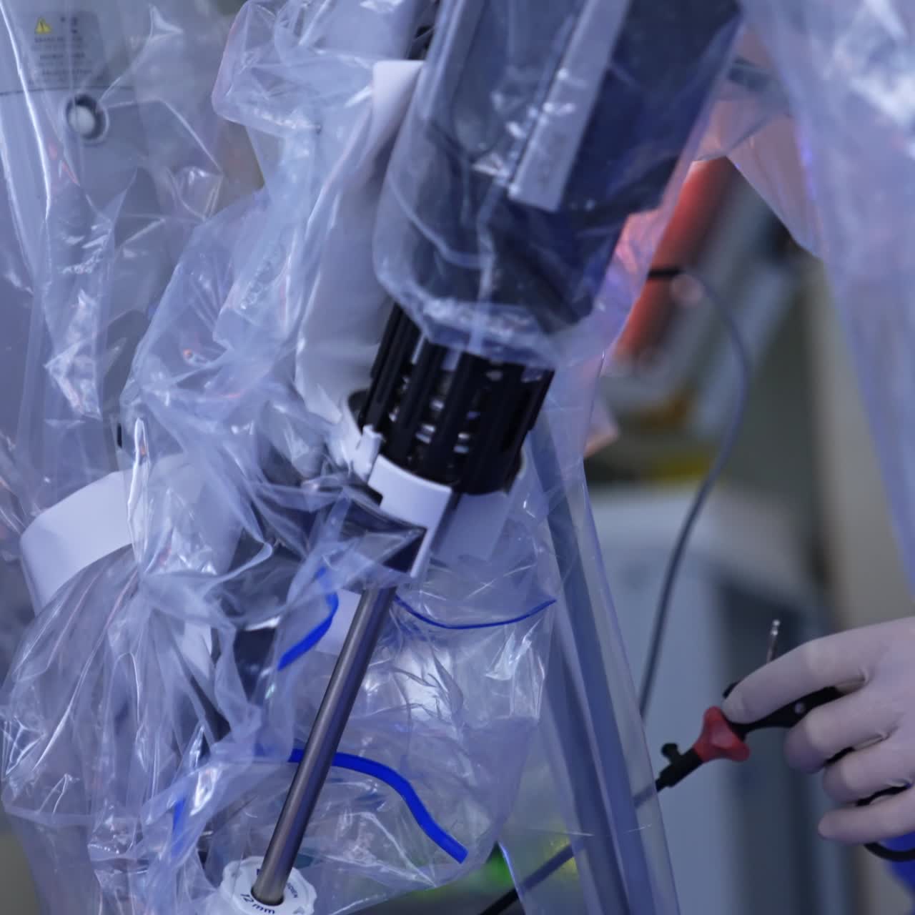 Robotic manipulator arms carry out laparoscopic procedure. Doctor standing nearby uses medical tools. Close up
