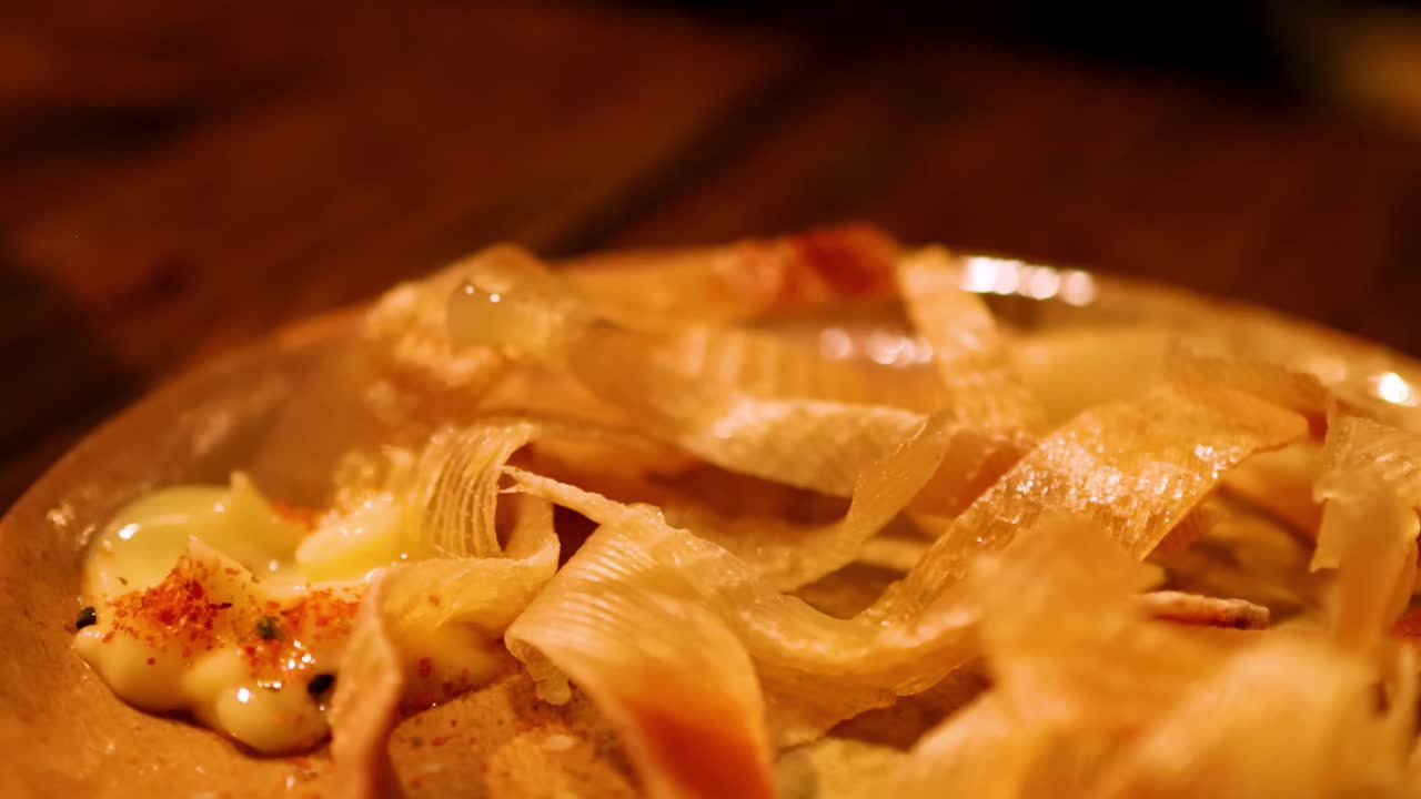Close-up of chopsticks interacting with a grilled dish topped with creamy sauce and spices.
