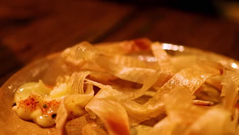close-up of chopsticks interacting with a grilled dish topped with creamy sauce and spices.