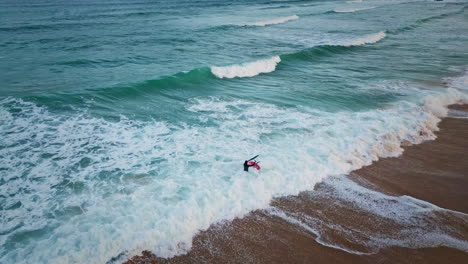 surfista desconocido entrando en el océano sosteniendo una tabla de surf en olas tormentosas vista aérea