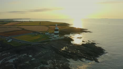 Aerial-view,-4K,-sunrise,-high-pan-left,-Hook-Lighthouse-is-situated-on-Hook-Head-at-the-tip-of-the-Hook-Peninsula-in-Co-Wexford,Ireland,-oldest-lighthouse-in-the-world,-was-built-in-the-12th-century