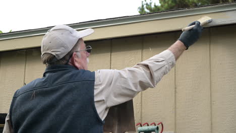 elderly senior man paints trim on shed with paint brush