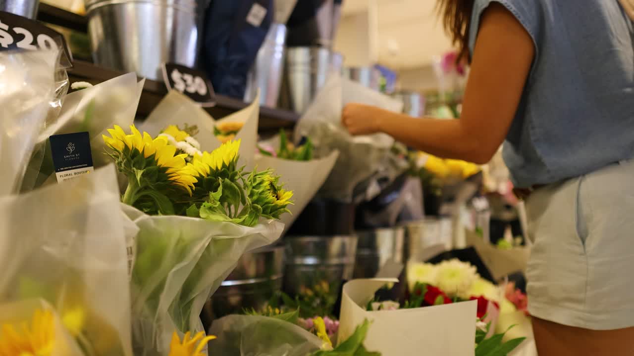 A woman selects flowers in a vibrant Gold Coast florist shop, with bright lighting and colorful blooms