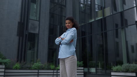 Cheerful-manager-standing-at-office-building-alone.-Content-businesswoman-smile