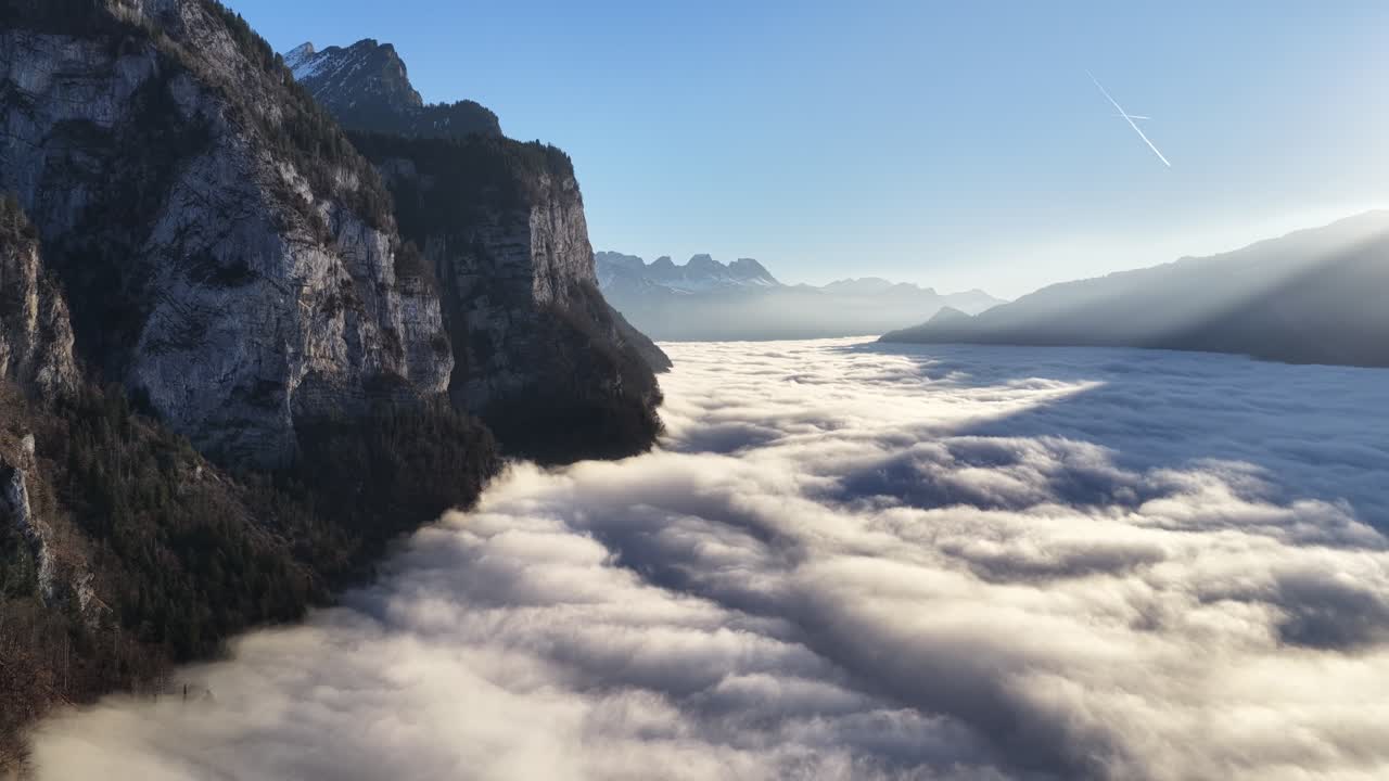 Alpi del Churfirsten, Svizzera, imponenti scogliere sopra un mare di nuvole ondeggianti mentre un drone si allontana su un'ampia valle alpina e un pacifico paesaggio mattutino