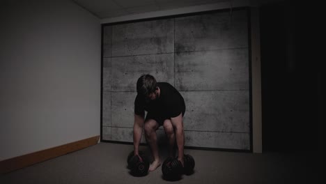 줄 위에 구부러진 덤벨, 영화적 조명, 검은색 체육복을 입은 백인 남자