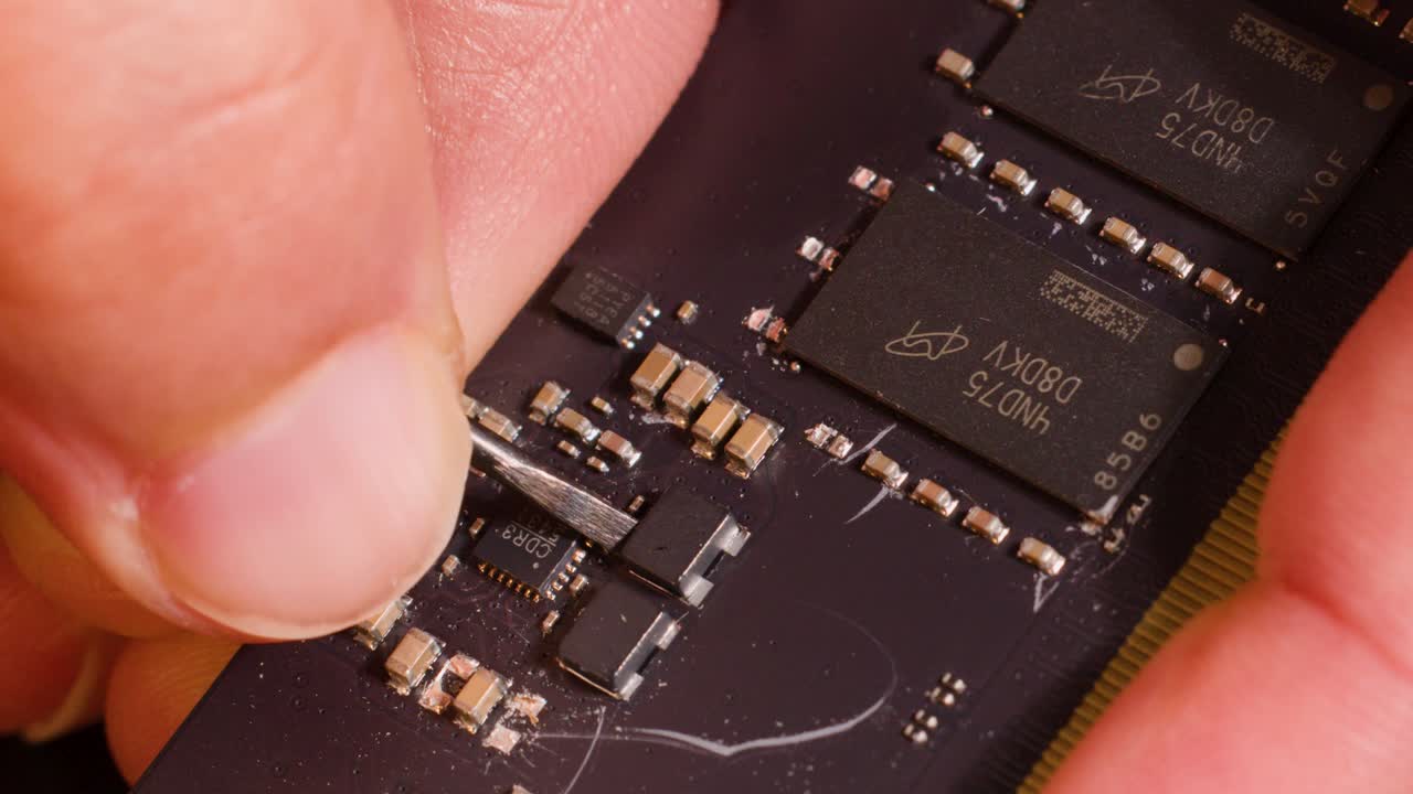 Close-up macro shot of hands using a metal tool to repair a computer memory module