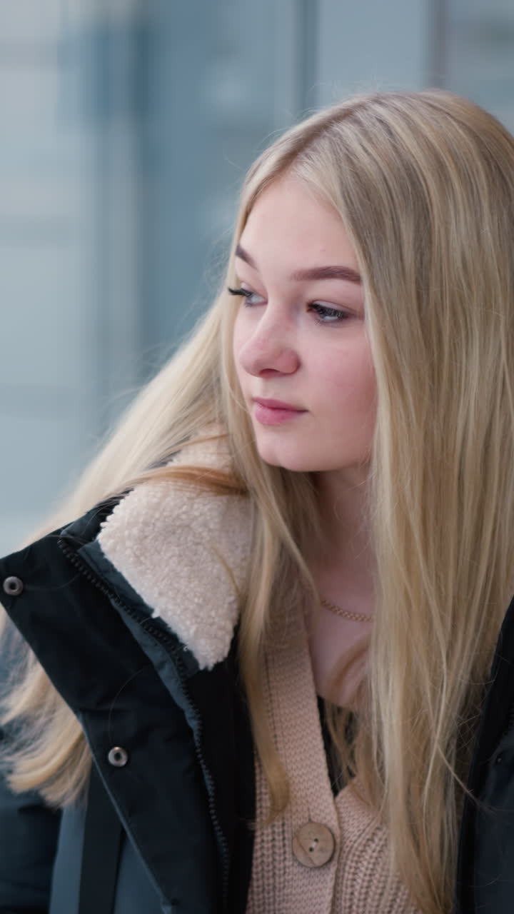 유리 벽을 가진 현대적인 건물에서 철 철로에 손을 고있는 여성은 미묘한 도시 배경과 자연 빛으로 상에 빠졌습니다.