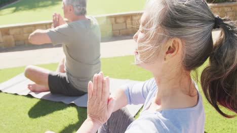 Happy-diverse-senior-couple-practicing-yoga-and-meditating-on-mats-in-garden